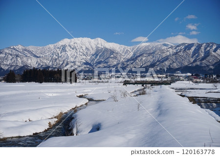 Scenery of the snow-covered Shonomata River and a train with blue skies and the silvery white Mount Hakkai in the background Ver2 Scenery of the snow-covered Shonomata River and a train with blue skies and the silvery white Mount Hakkai in the background Ver2 120163778
