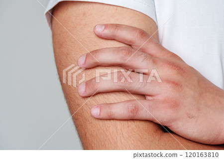 A person standing sideways wearing a casual white t-shirt and dark pants with a hand resting A person standing sideways wearing a casual white t-shirt and dark pants with a hand resting 120163810