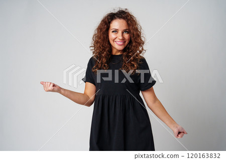 A young woman stands confidently in a black dress, showcasing a playful pose against a plain background A young woman stands confidently in a black dress, showcasing a playful pose against a plain background 120163832