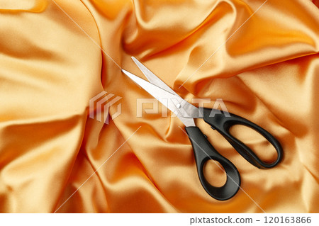 Scissors resting on a vibrant orange satin fabric, perfect for crafting or sewing projects Scissors resting on a vibrant orange satin fabric, perfect for crafting or sewing projects 120163866