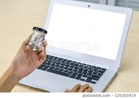 Closeup hand holding glass pill packer bottle with cap in front of white screen laptop computer. Closeup hand holding glass pill packer bottle with cap in front of white screen laptop computer. 120163919
