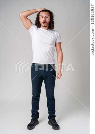 A man with curly hair expresses surprise while looking upwards in a neutral background 120163937