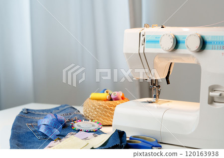 Sewing machine in use on a wooden table, stitching a light fabric in a well-lit indoor workspace Sewing machine in use on a wooden table, stitching a light fabric in a well-lit indoor workspace 120163938