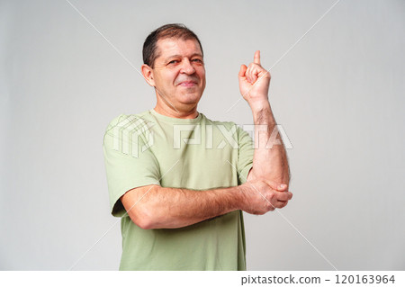 A middle-aged man with a thoughtful expression gestures with one finger raised while standing against a plain background 120163964