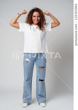 Young woman joyfully celebrates in casual attire against a neutral background Young woman joyfully celebrates in casual attire against a neutral background 120163985