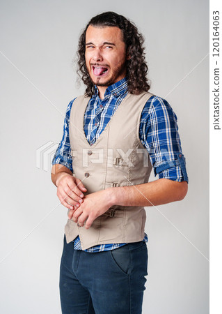 Man making a silly face with tongue out in casual attire against a neutral background 120164063