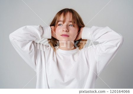 Young woman in a casual white long-sleeve shirt and loose denim pants poses against a light gray background Young woman in a casual white long-sleeve shirt and loose denim pants poses against a light gray background 120164066