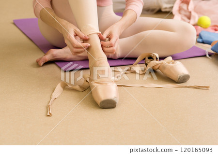 Ballet dancer sitting on floor, preparing pointe shoes before practice. 120165093