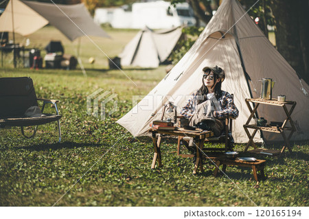 Young woman wearing sunglasses sitting in front of a tent 120165194