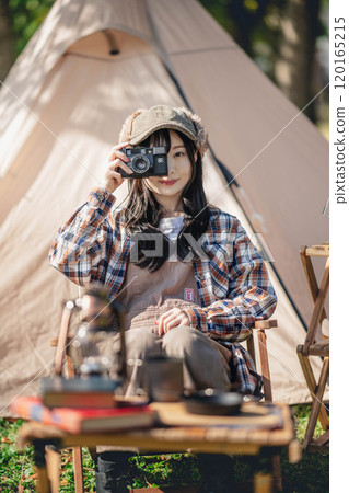 A young woman sitting in front of a tent and holding a camera 120165215