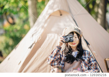 A young woman sitting in front of a tent and holding a camera 120165216