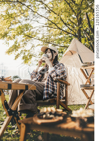 A woman resting in a chair at a campsite, drinking a drink A woman resting in a chair at a campsite, drinking a drink 120165356