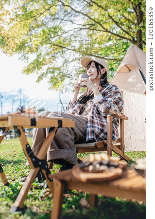 A woman resting in a chair at a campsite, drinking a drink 120165359