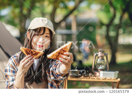Woman eating at a campsite Woman eating at a campsite 120165379