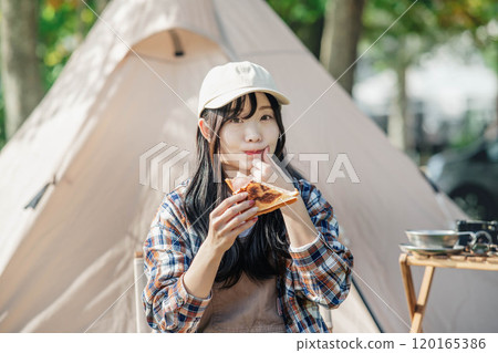 Woman eating at a campsite 120165386