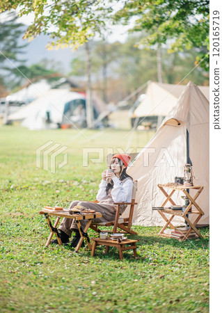 A woman taking a break at a campsite while eating and drinking 120165719