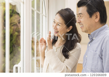 成熟的夫婦透過窗戶看著他們的孫子，在外面揮手致意 120166809