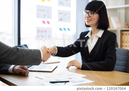 Business woman shaking hands with colleague in modern office setting 120167004
