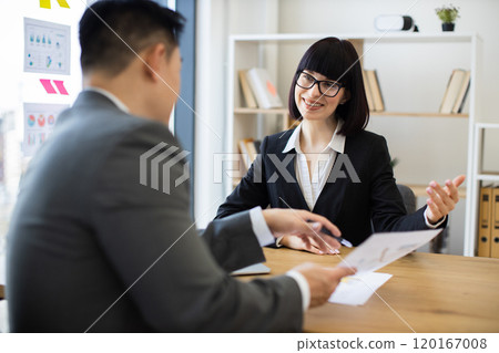 Asian businessman presents report to Caucasian businesswoman in meeting Asian businessman presents report to Caucasian businesswoman in meeting 120167008