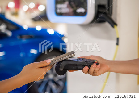 Person makes a contactless payment at a terminal near a charging station with a mobile device. Person makes a contactless payment at a terminal near a charging station with a mobile device. 120167021