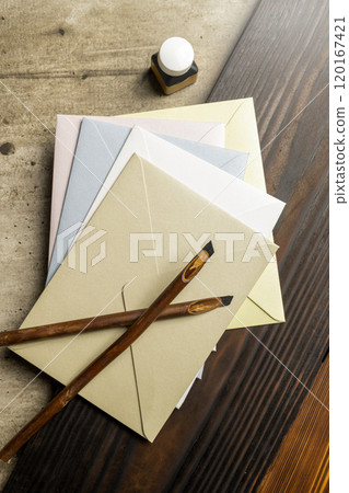 Two calligraphy reeds covered ink with inkwell and stack of envelopes on the table 120167421