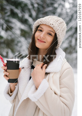 Young woman holding cup of hot chocolate and smiling enjoying her drink 120167959