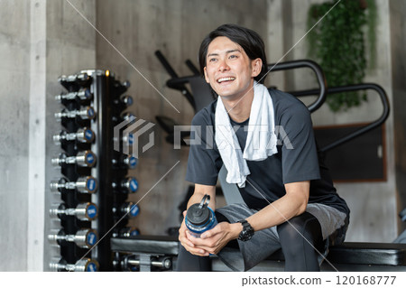 Young Asian man taking interval breaks at the gym (hydration/protein) 120168777