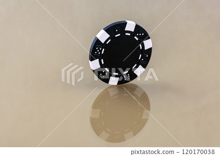 A black casino chip stands on the reflecting surface 120170038