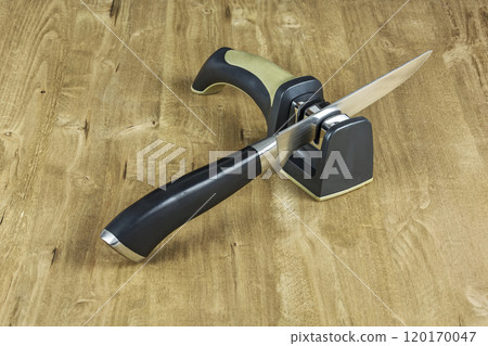 On the wooden surface there is a sharpener and a metal knife with a plastic handle On the wooden surface there is a sharpener and a metal knife with a plastic handle 120170047