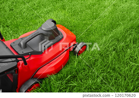 An electric red and black lawnmower mows green grass. Work near your home in the garden. 120170620