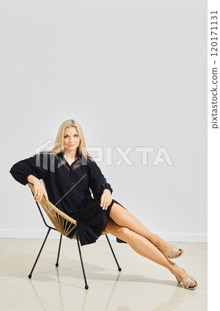 Fashionable woman in loose black dress posing on a modern chair Fashionable woman in loose black dress posing on a modern chair 120171131
