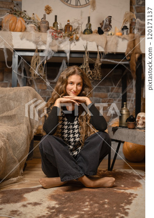Cozy indoor Halloween setup with a woman sitting casually surrounded by autumn decorations Cozy indoor Halloween setup with a woman sitting casually surrounded by autumn decorations 120171137