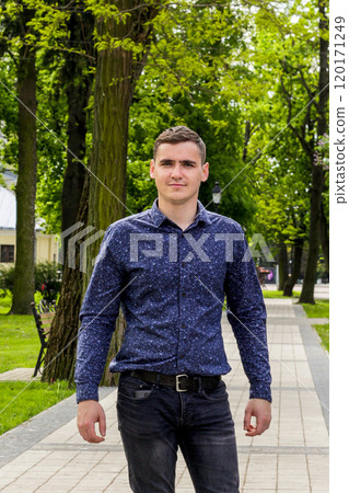 A young man in his early 20s standing in a park, captured in a vertical format. The natural setting is lush and green, with trees and grass providing a peaceful background A young man in his early 20s standing in a park, captured in a vertical format. The natural setting is lush and green, with trees and grass providing a peaceful background 120171249