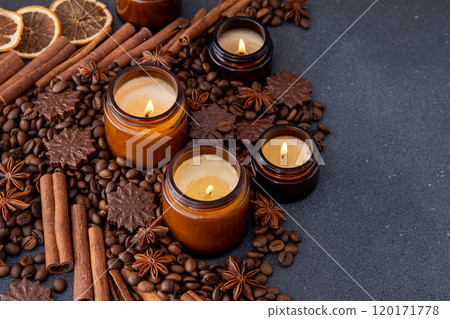 Soy scented candle in a jar. Coffee beans, anise, cinnamon spices. The candles are burning. Dark background. Soy scented candle in a jar. Coffee beans, anise, cinnamon spices. The candles are burning. Dark background. 120171778