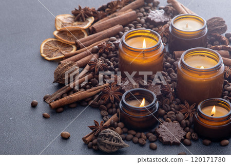 Soy scented candle in a jar. Coffee beans, anise, cinnamon spices. The candles are burning. Dark background. 120171780