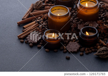 Soy scented candle in a jar. Coffee beans, anise, cinnamon spices. The candles are burning. Dark background. Soy scented candle in a jar. Coffee beans, anise, cinnamon spices. The candles are burning. Dark background. 120171783