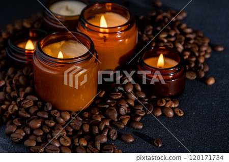 Soy scented candle in a jar. Coffee beans, anise, cinnamon spices. The candles are burning. Dark background. Soy scented candle in a jar. Coffee beans, anise, cinnamon spices. The candles are burning. Dark background. 120171784