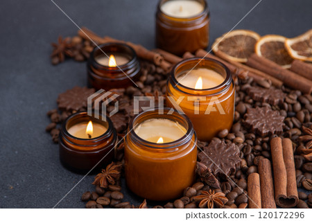 Soy scented candle in a jar. Coffee beans, anise, cinnamon spices. The candles are burning. Dark background. Soy scented candle in a jar. Coffee beans, anise, cinnamon spices. The candles are burning. Dark background. 120172296