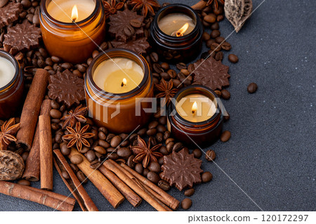 Soy scented candle in a jar. Coffee beans, anise, cinnamon spices. The candles are burning. Dark background. Soy scented candle in a jar. Coffee beans, anise, cinnamon spices. The candles are burning. Dark background. 120172297