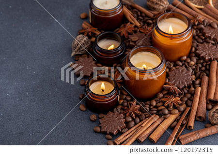 Soy scented candle in a jar. Coffee beans, anise, cinnamon spices. The candles are burning. Dark copy space background. Soy scented candle in a jar. Coffee beans, anise, cinnamon spices. The candles are burning. Dark copy space background. 120172315