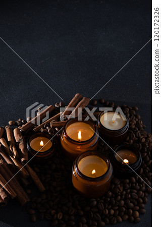 Soy scented candle in a jar. Coffee beans, anise, cinnamon spices. The candles are burning. Dark copy space background. 120172326