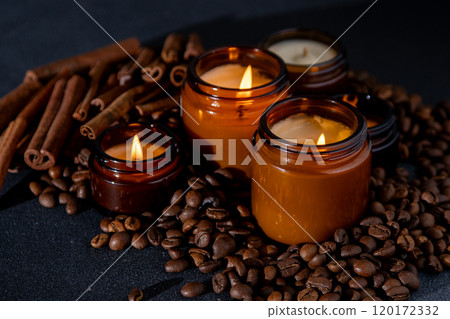 Soy scented candle in a jar. Coffee beans, anise, cinnamon spices. The candles are burning. Dark background. Soy scented candle in a jar. Coffee beans, anise, cinnamon spices. The candles are burning. Dark background. 120172332