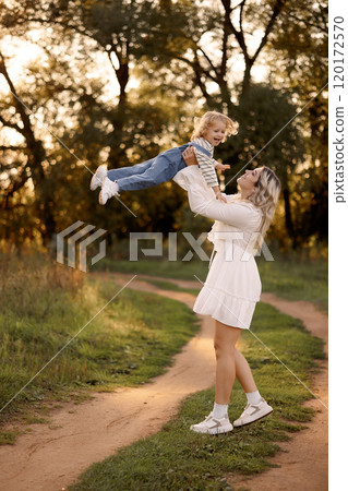 Happy Caucasian mother holding her baby in the air on a walk in a summer park Happy Caucasian mother holding her baby in the air on a walk in a summer park 120172570