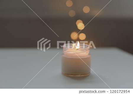 Cozy home interior decor, burning candle on table against blurred lights. Handmade scented soy wax candle in a glass. space for text.  120172954