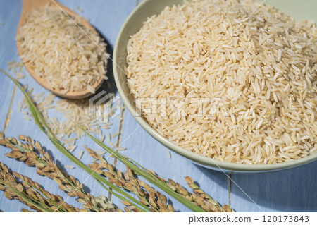 A bowl is filled with brown rice is to next spoon and ears of rice 120173843