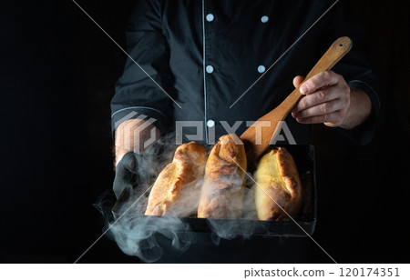 Warm, steamy loaves of bread are freshly baked and held by a chef in a dark kitchen. The golden crust reflects the joy of culinary craftsmanship and passion for baking 120174351