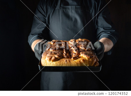 A skilled baker proudly holds a tray of freshly baked cinnamon rolls, their golden-brown surface glistening. The warm pastry exudes a delightful aroma, tempting anyone nearby A skilled baker proudly holds a tray of freshly baked cinnamon rolls, their golden-brown surface glistening. The warm pastry exudes a delightful aroma, tempting anyone nearby 120174352