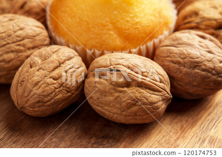 Fresh baked muffin surrounded by raw whole organic walnuts on a wooden surface, showcasing a natural wholesome snack. Close up Fresh baked muffin surrounded by raw whole organic walnuts on a wooden surface, showcasing a natural wholesome snack. Close up 120174753