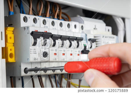 Electrician Testing Circuit Breaker with Red Handle Screwdriver 120175889
