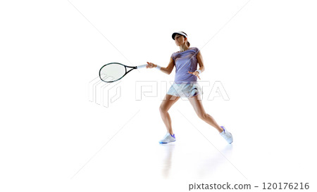Tennis player stands poised holding racket ready, her expression intense as she prepares for next hit against white studio background. 120176216